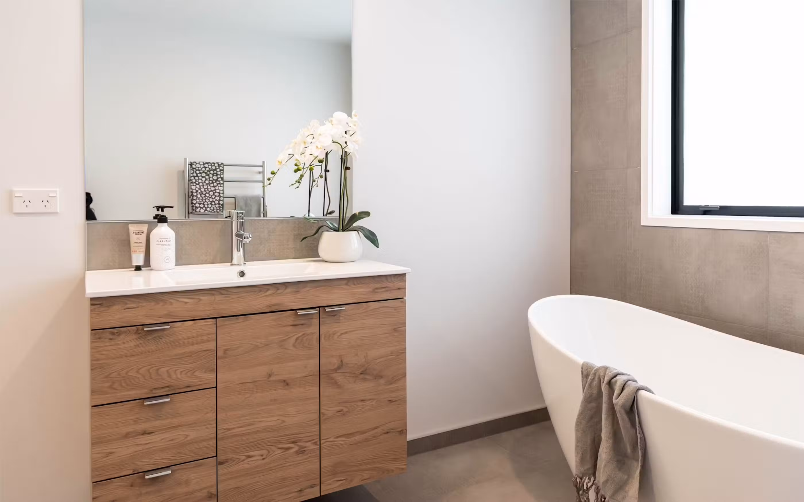 A contemporary bathroom featuring warm timber cabinetry, modern finishes and a freestanding bath.