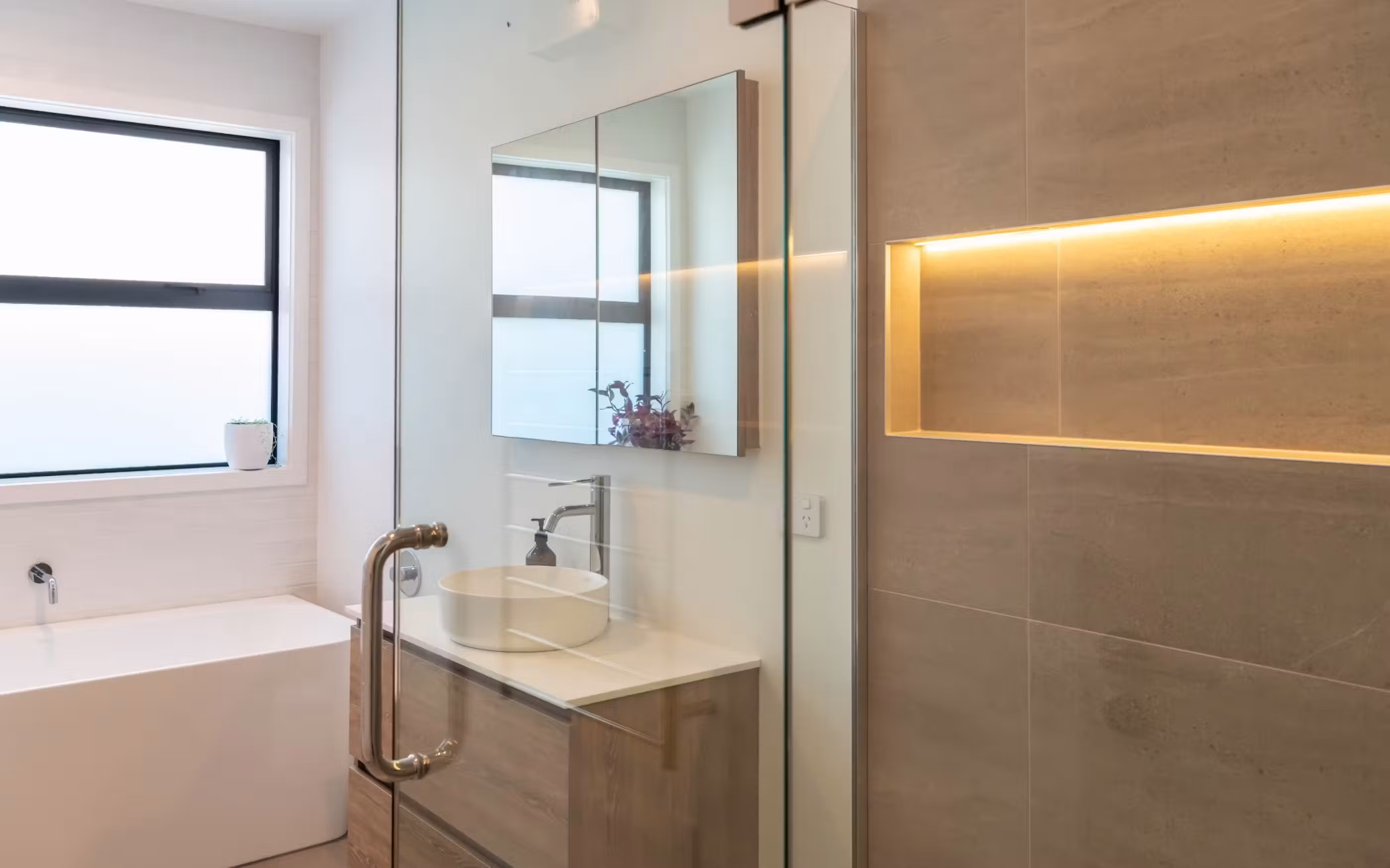 A contemporary bathroom featuring sleek finishes, warm timber cabinetry and thoughtful integrated lighting